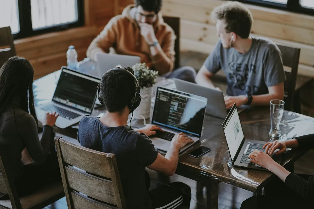 A team works on laptops around a table, seen from above