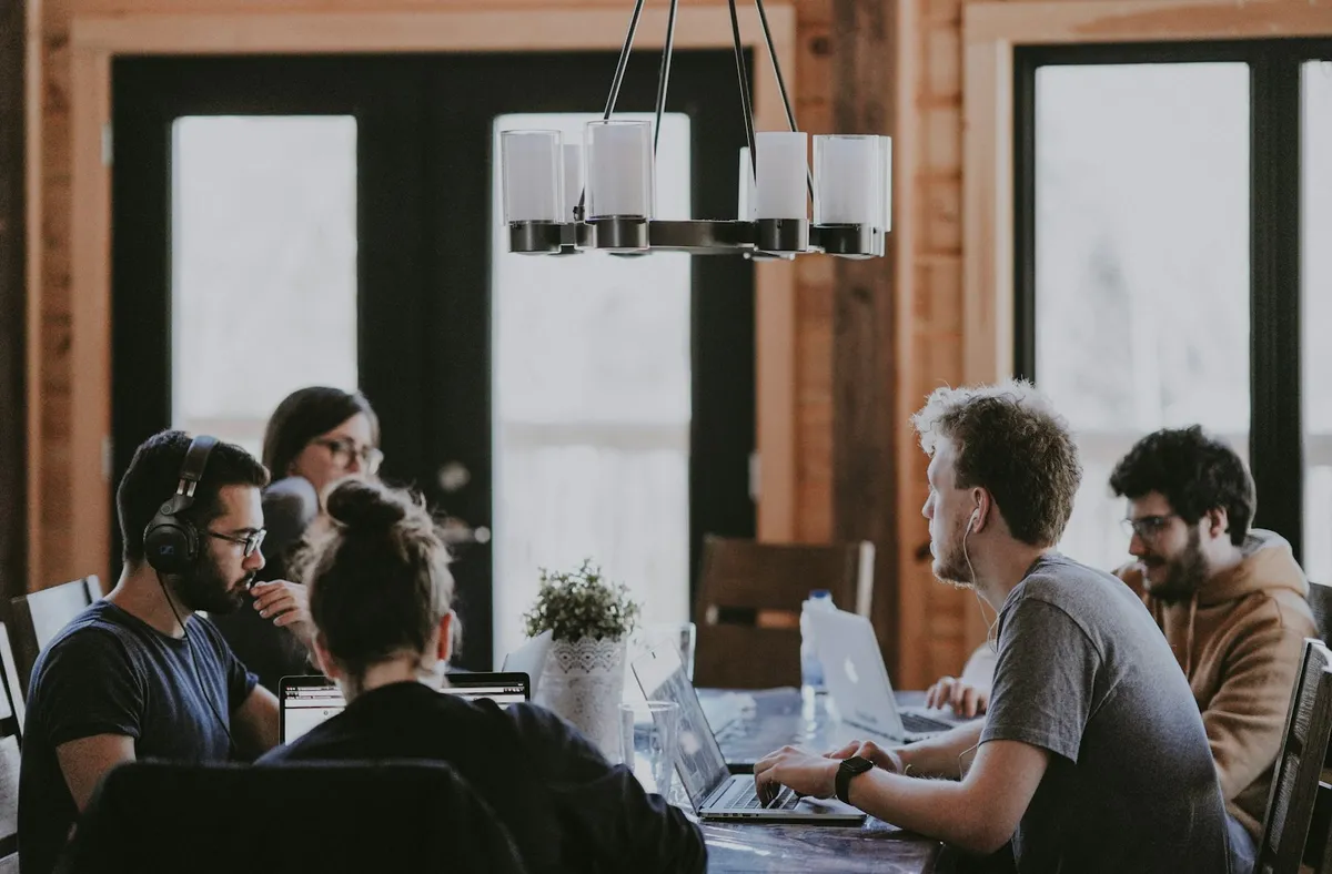 Four people work on laptops at a wooden table