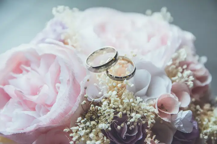 Wedding details: flowers and rings on a pale surface